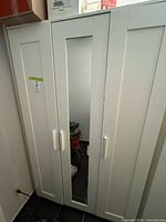 Frontal view of entire white 3-door wardrobe showing mirror door and handles