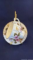 Cup resting in saucer on metal stand showing floral pattern and gold trim
