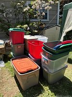 Stacked assortment of colored and clear plastic totes with lids outdoors