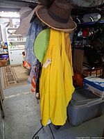 Rack showing yellow raincoat, multiple straw hats, patterned scarves