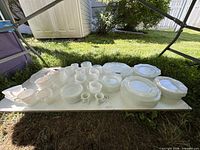 Full grouping of stacked milk glass dinnerware pieces on board outdoors