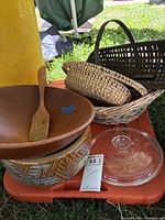 Group shot of all items stacked on orange surface: wooden bowl with spatula, ceramic bowl, glass lid, three baskets