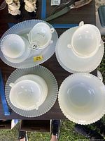 Stacked milk glass plates and double-handled cups showing fluted ribbing and scalloped rims