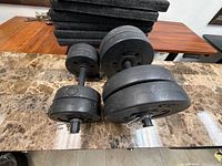Two assembled adjustable dumbbells with multiple black plates on marble surface