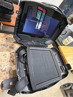 Open GAEMS G155 case showing powered-on screen, interior console tray and strap