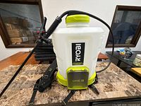 Front view of Ryobi backpack sprayer with wand, hose and straps visible