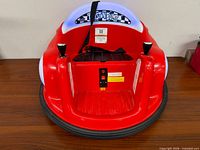 Front view of red Twist 'N Bump bumper car showing seat, joysticks, harness, charge port and labels