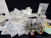 Wide view of loose stamps, glassine envelopes, and Stamp Finder booklet spread on black surface