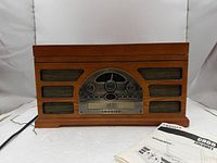Front view of Crosley CR66 showing control panel, speaker grilles, attached power cord, and manual