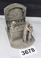 Front angled view of entire pewter shooting gallery sculpture with attendant, man, girl, counter, backdrop