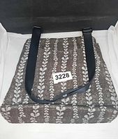 Front view of square fabric handbag with vine pattern and black adjustable strap