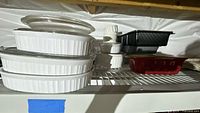 Stacked white ceramic casserole dishes with glass lids shown
