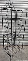 Full view of black metal folding shelf showing three shelves and decorative scrollwork