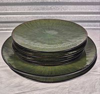 Stack of all four green textured dinner plates showing face design and brown rim