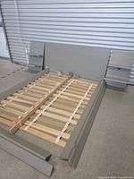 Disassembled bed frame laid out: headboard, nightstands attached, side rails, footboard, slats