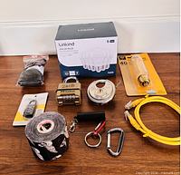 All items grouped: LED bulb box, yellow cable, two padlocks, combination lock package, tape roll, socks pack, carabiners, storage tube, packaged strap