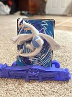 Front view of Lugia figure on purple base with card inserted