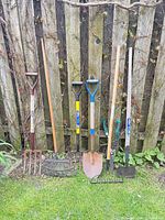 Eight garden tools lined up against fence