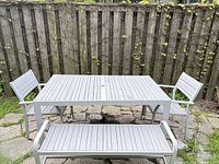 Front view of complete patio set: table, bench, two chairs against fence