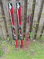 Full view of both Nordica skis and Atomic poles leaning against fence