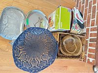 Top view of baskets, metal trays, blue crocheted bowl and boxed Takeya iced tea maker