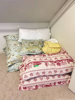 Full grouping of blankets, sheet set and pillows stacked on floor