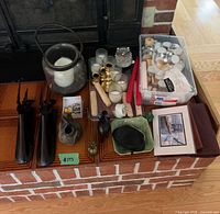 Group of candles, holders, figurines, wallets and art on hearth