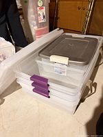 Stack of three Sterilite 60 Qt bins with purple latch lids, grey-lidded 25 Qt bin nested, lid-less bin below