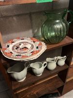 Shelf with plates, green glass pitcher, three matte green creamers