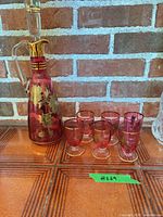 Cranberry Bohemian decanter with stopper and six cordial glasses on tiled surface