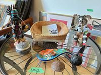 Entire lot on glass table showing Kachina dolls, basket, seed pots, ceramic rest