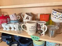 Entire assortment on cabinet shelf showing mugs, egg cups, glasses, tumblers, teapot