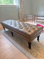 Full view of grey tufted leather ottoman bench on rug