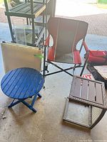 Overview of blue side table, brown wicker side table, red folding chair and folded white table