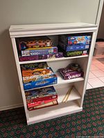 Front view of white bookshelf with three shelves and games for scale