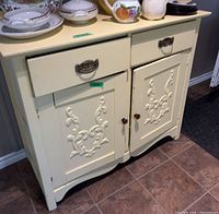 Front view of pastel yellow cabinet showing drawers, carved doors, hardware