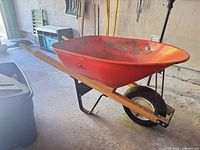 Left side view of wheelbarrow showing red tray, wood handles, tire, and support frame