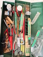 Overview of green toolbox interior with assorted tools, cutters, goggles and adhesive cans