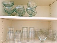 Pedestal dessert cups stacked on upper shelf, tumblers and wavy bowls on lower shelf