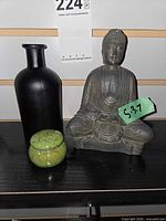Group shot of Buddha statue, dark glass vase, green ceramic box