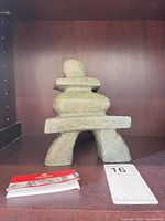 Front view of stone inukshuk sculpture on shelf with card and lot tag visible