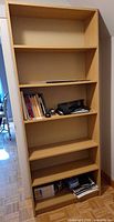 Full frontal view of tall light oak laminate bookcase with contents shown for scale