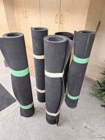 Four rolled black rubber mats standing upright on concrete floor