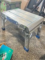 Side view of aluminum folding utility step stool showing platform, folding legs, blue caps