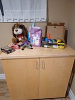 All items together on cabinet top: card game boxes, three plush toys, bowling set in case, bag with Easter eggs