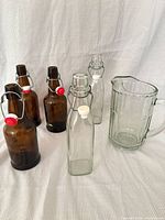 group shot of 3 amber bottles, 2 clear bottles, and clear pitcher