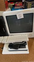 Front view of Apple iMac G3 with Apple keyboard resting on MacBook and additional devices