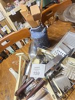 Group of utensils on table with crock and numbered tag visible