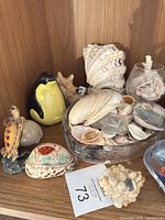 Overview showing penguin figurine, turtle figurine, glass bowl with shells, painted cowrie shell, resin shell ornament, large shell cluster, glass container with shells