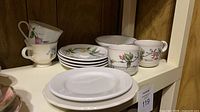 Shelf view of vine-pattern cups, saucers, bowls and white plates